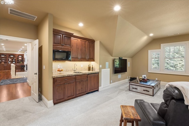 kitchen with lofted ceiling, sink, light stone countertops, black microwave, and light carpet