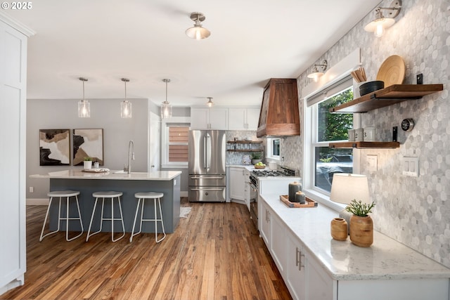 6126 SE 23rd Ave, Portland, OR 97202 - kitchen featuring stainless steel appliances, open shelves, wood finished floors, premium range hood, and a kitchen breakfast bar