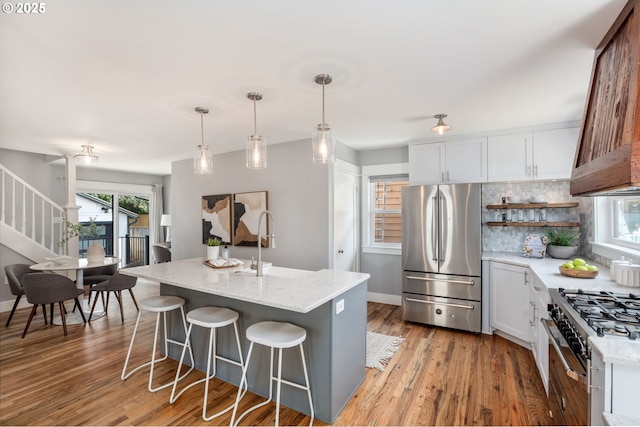 6126 SE 23rd Ave, Portland, OR 97202 - kitchen featuring stainless steel appliances, tasteful backsplash, light stone countertops, custom range hood, and light wood finished floors