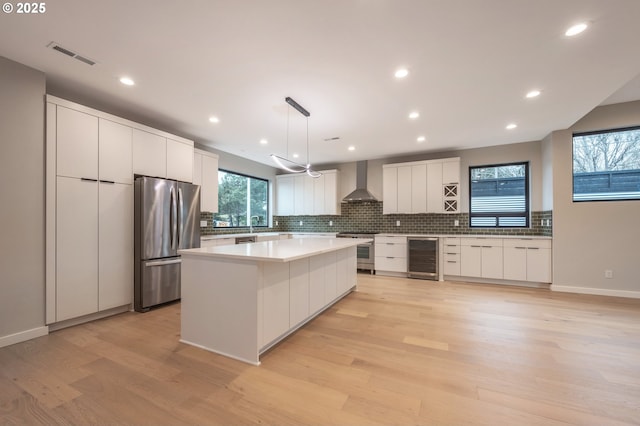 kitchen featuring pendant lighting, wall chimney range hood, stainless steel appliances, white cabinets, and a kitchen island