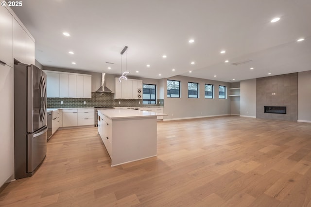 kitchen featuring decorative light fixtures, appliances with stainless steel finishes, a kitchen island, wall chimney range hood, and white cabinets