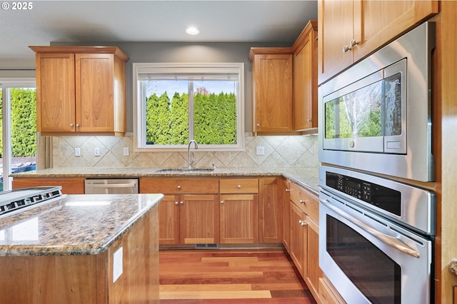 kitchen featuring a sink, plenty of natural light, light stone counters, and stainless steel appliances