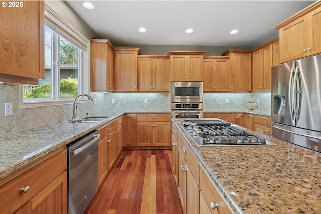 kitchen featuring light stone counters, decorative backsplash, stainless steel appliances, a sink, and wood finished floors