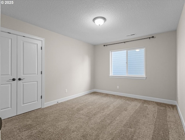 carpeted empty room featuring baseboards, visible vents, and a textured ceiling