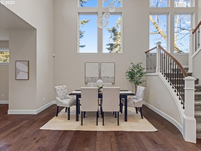 dining area featuring stairway, baseboards, a towering ceiling, dark wood-type flooring, and an inviting chandelier