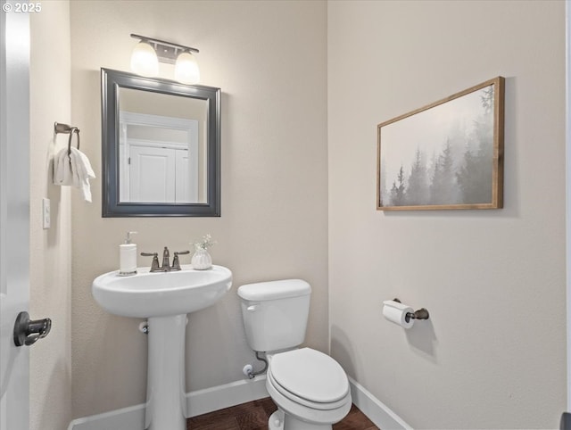 half bathroom with baseboards, toilet, and a sink
