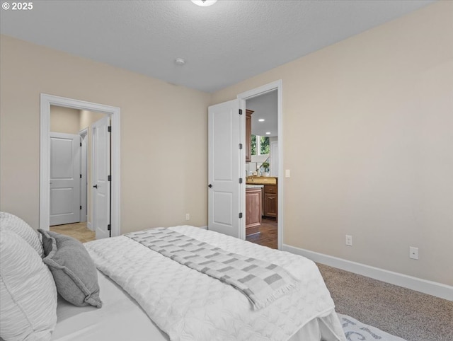 bedroom with ensuite bathroom, baseboards, carpet, and a textured ceiling