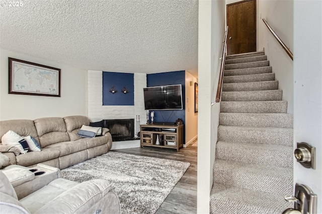 living room featuring a large fireplace, stairway, wood finished floors, and a textured ceiling