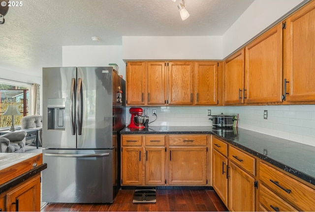 kitchen with dark stone countertops, backsplash, stainless steel fridge, and dark wood-style flooring