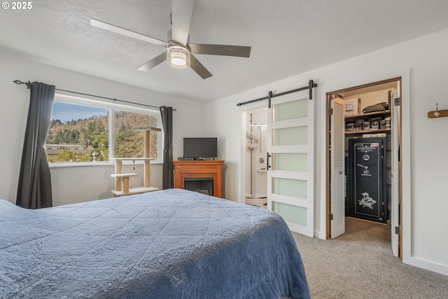 bedroom with a ceiling fan, carpet, a textured ceiling, a walk in closet, and a barn door