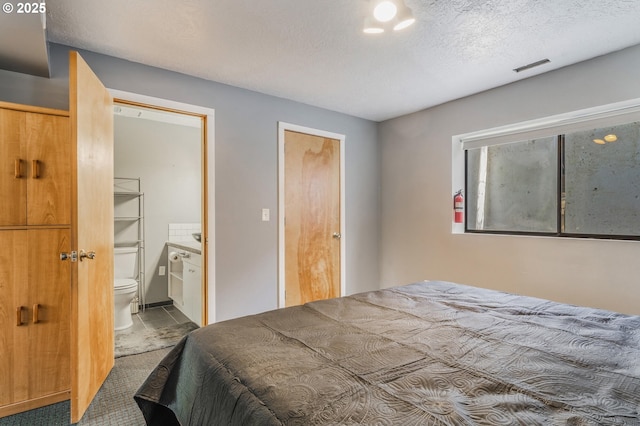 bedroom with visible vents, connected bathroom, a textured ceiling, and carpet flooring