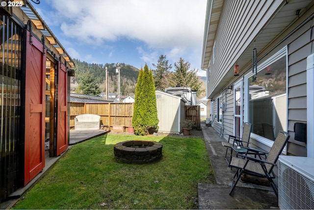 view of yard featuring an outbuilding, central AC unit, fence, a shed, and a fire pit