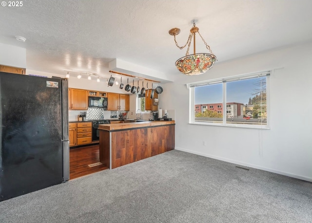 kitchen featuring visible vents, brown cabinets, a peninsula, black appliances, and tasteful backsplash