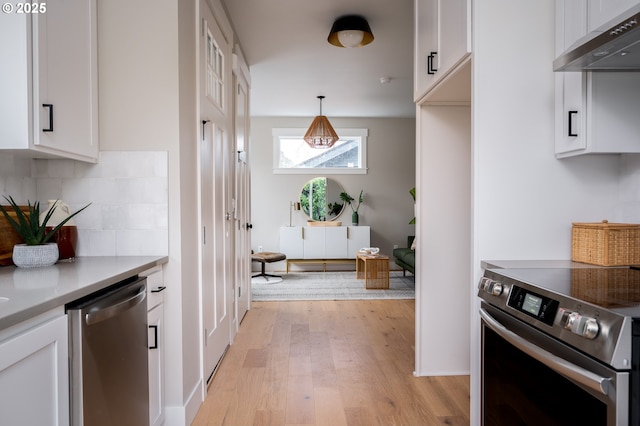 kitchen with white cabinetry, light wood-type flooring, wall chimney range hood, pendant lighting, and appliances with stainless steel finishes