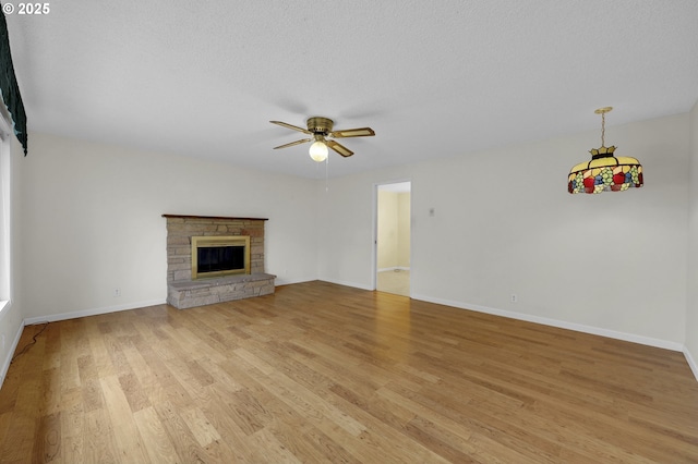 unfurnished living room featuring baseboards, a stone fireplace, a ceiling fan, and light wood-style flooring