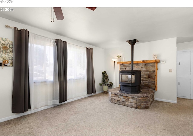 carpeted living room featuring ceiling fan and a wood stove