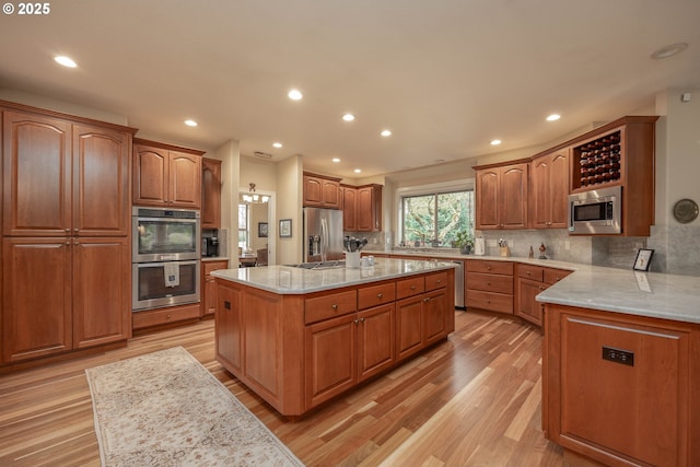 kitchen with appliances with stainless steel finishes, light wood-style floors, brown cabinetry, backsplash, and a kitchen island