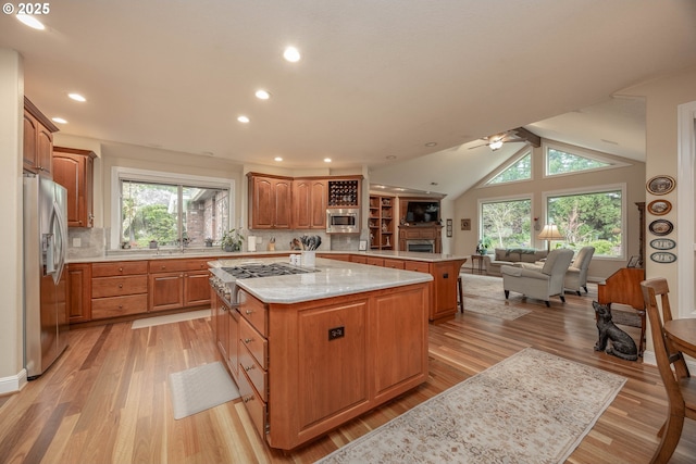 kitchen with a peninsula, a ceiling fan, a kitchen island, stainless steel appliances, and open floor plan