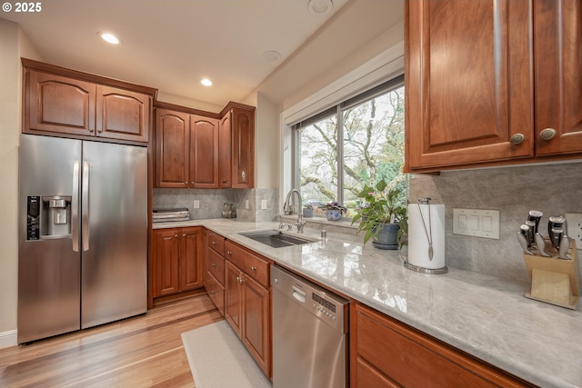 kitchen with a sink, light wood finished floors, light stone countertops, decorative backsplash, and stainless steel appliances