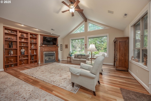 living room featuring visible vents, ceiling fan, a high end fireplace, beam ceiling, and light wood-style flooring
