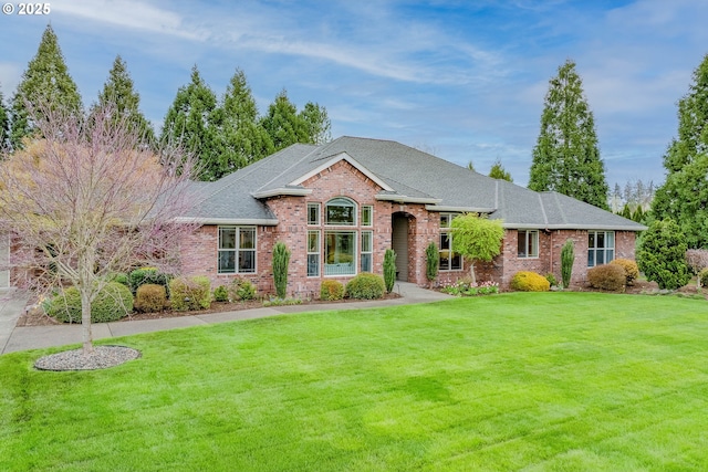 view of front of home with a shingled roof, brick siding, and a front lawn