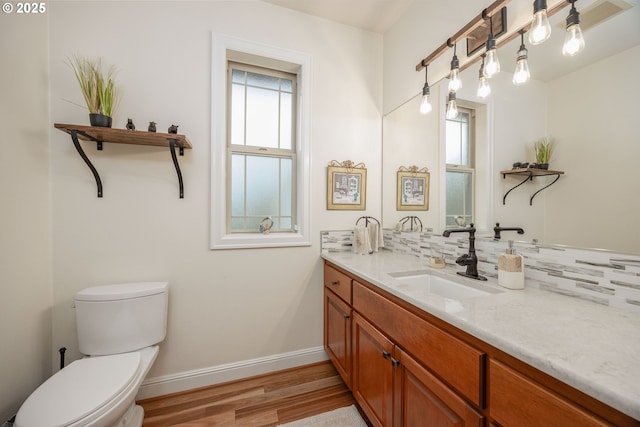 bathroom with baseboards, toilet, vanity, wood finished floors, and backsplash
