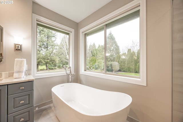 bathroom featuring a soaking tub, a healthy amount of sunlight, vanity, and baseboards
