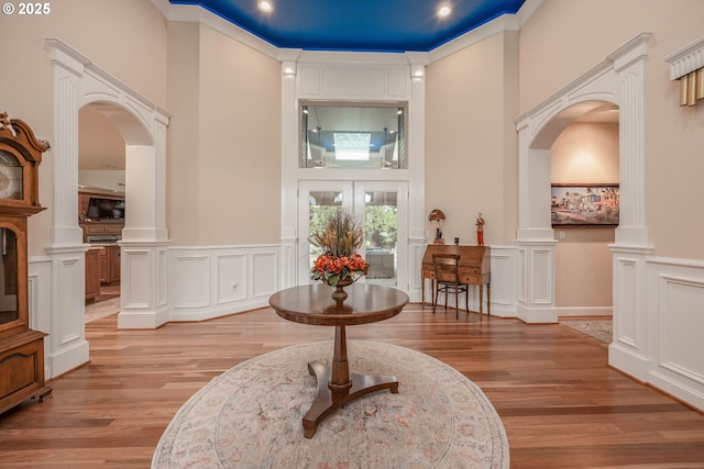 entrance foyer with a decorative wall, decorative columns, light wood-type flooring, arched walkways, and wainscoting