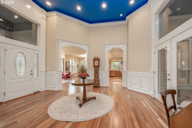 entryway with arched walkways, a high ceiling, ornate columns, and light wood-type flooring