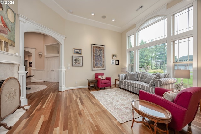 living area with a high ceiling, light wood-style floors, visible vents, decorative columns, and arched walkways