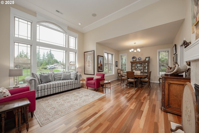 living room with a towering ceiling, baseboards, an inviting chandelier, light wood-style floors, and visible vents