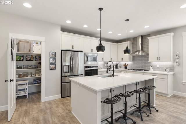 16290 SE Eckert Ln, Damascus, OR 97089 - kitchen with stainless steel appliances, wall chimney exhaust hood, light wood finished floors, tasteful backsplash, and an island with sink