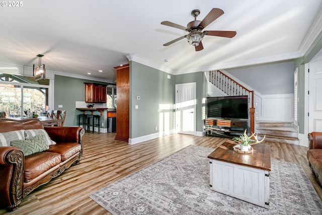 living room with ceiling fan with notable chandelier, light hardwood / wood-style flooring, and ornamental molding