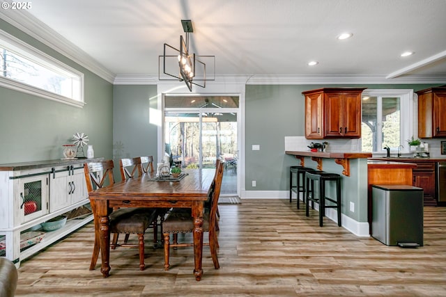 dining room featuring an inviting chandelier, sink, crown molding, and light hardwood / wood-style floors