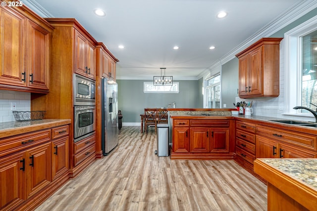 kitchen with sink, stainless steel appliances, tasteful backsplash, decorative light fixtures, and light wood-type flooring