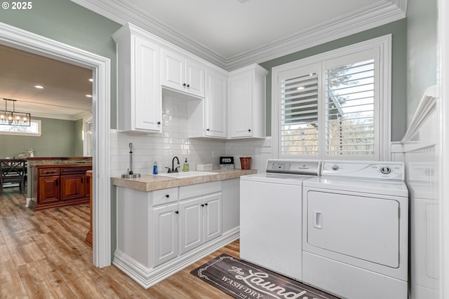 laundry room featuring sink, crown molding, cabinets, washing machine and clothes dryer, and light wood-type flooring