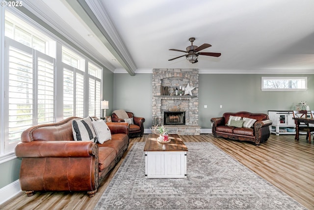 living room with crown molding, wood-type flooring, a stone fireplace, and ceiling fan