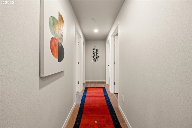hall featuring baseboards, wood finished floors, and recessed lighting