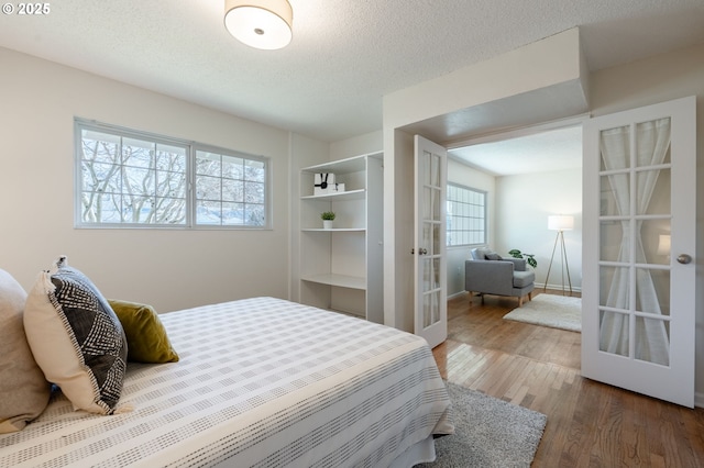 bedroom with multiple windows, hardwood / wood-style floors, a textured ceiling, and french doors