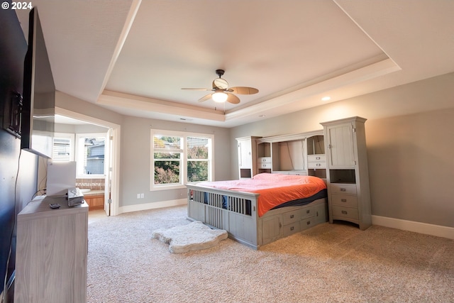 carpeted bedroom featuring a raised ceiling, ceiling fan, and ensuite bathroom