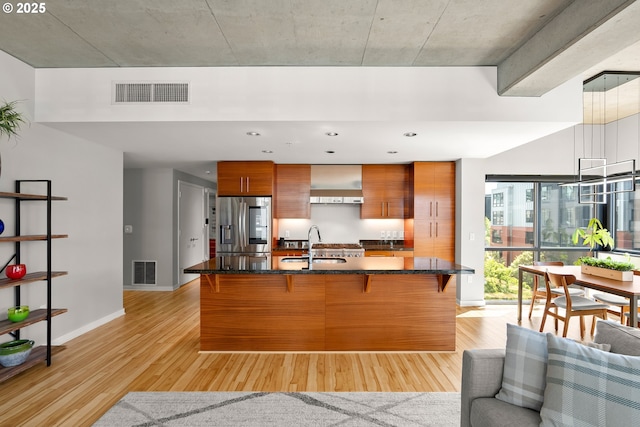 1830 NW Riverscape St Unit 406, Portland, OR 97209 - kitchen with a breakfast bar, stainless steel fridge, a sink, brown cabinetry, and visible vents