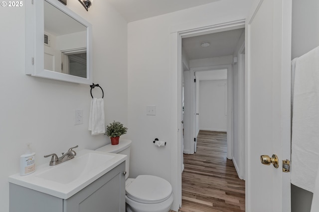half bathroom with toilet, baseboards, vanity, and wood finished floors