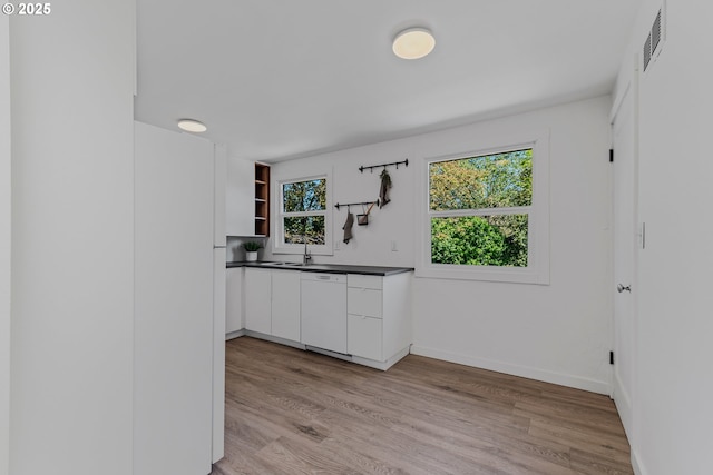 kitchen featuring light wood-style flooring, open shelves, dark countertops, visible vents, and white dishwasher