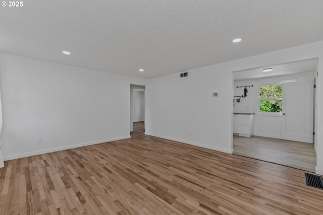 unfurnished living room with light wood-type flooring, baseboards, and visible vents
