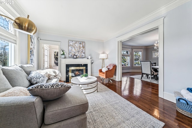 living room with crown molding, a fireplace, dark wood-style floors, a chandelier, and baseboards
