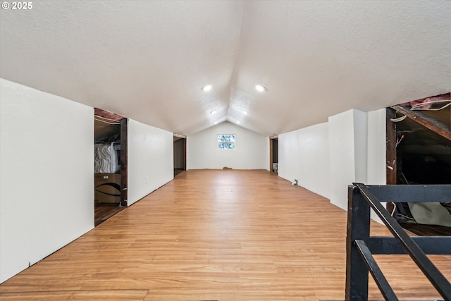 bonus room featuring lofted ceiling, light wood-type flooring, and a textured ceiling