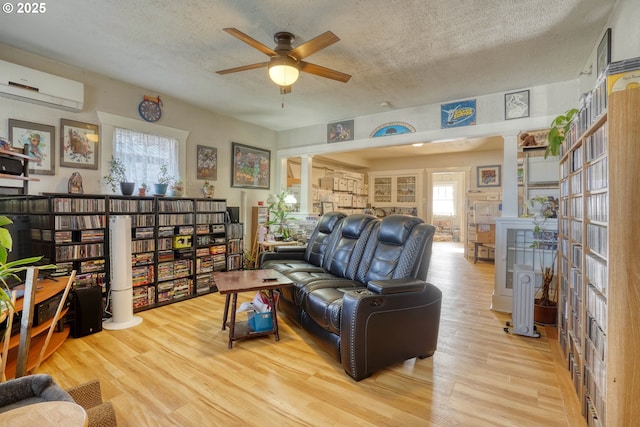 living room featuring ornate columns, a wall mounted air conditioner, a textured ceiling, and light hardwood / wood-style floors