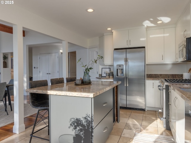 kitchen with light tile patterned flooring, a kitchen island, white cabinetry, a kitchen breakfast bar, and stainless steel appliances