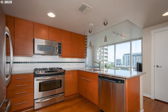 kitchen featuring visible vents, a peninsula, a sink, decorative backsplash, and appliances with stainless steel finishes