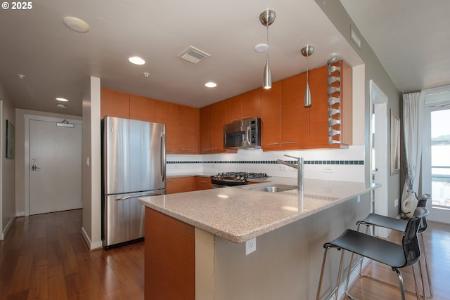 kitchen featuring a sink, appliances with stainless steel finishes, a peninsula, decorative backsplash, and dark wood-style flooring